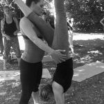 Doris Schernthaner hilft einer Yoga-Studentin von hinten auf einer Matte den Handstand zu halten. Im Garten. schwarz-weiß